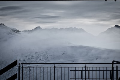 白天白雪覆盖的山附近的黑色金属栅栏
